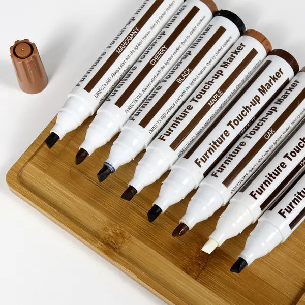 Lot de sept stylos de retouche de peinture pour réparation de meubles en bois avec fûts blancs et étiquettes brunes, dans des teintes assorties, incluant acajou, cerisier, noir, érable, chêne et beige, pour la retouche des meubles et la restauration des rayures.