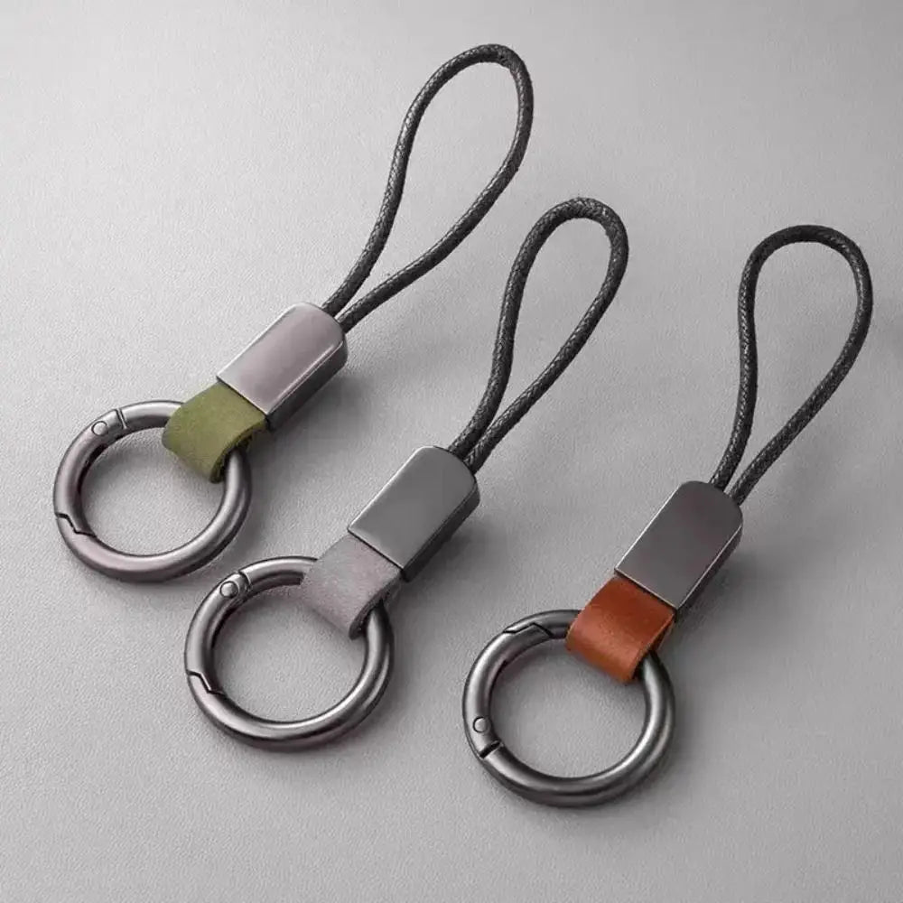 Three sleek metallic leather braided carabiner keychains feature a braided black cord and contrasting leather straps in olive green gray and tan.