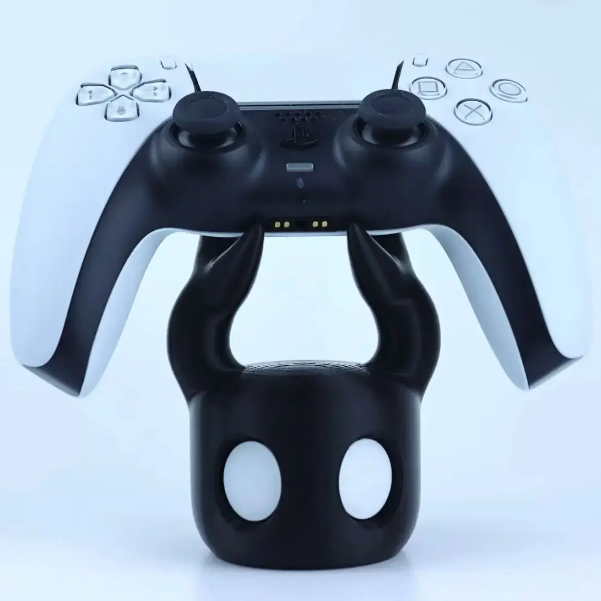 Black devil-themed hollow knight game controller stand in black holding a white and black PlayStation 5 DualSense controller.