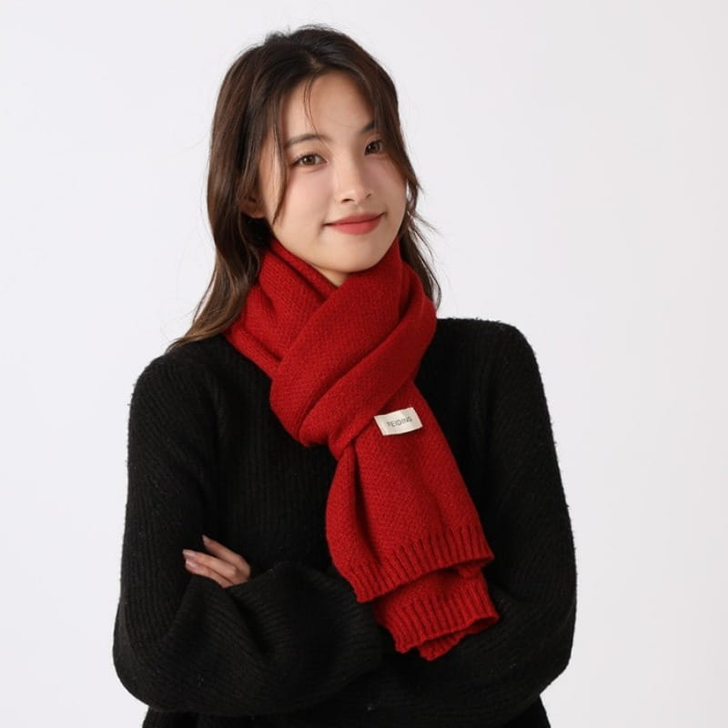 Una bufanda de invierno tejida en rojo, vibrante, para hombres y mujeres, con textura acanalada y una pequeña etiqueta blanca que se lleva alrededor del cuello.