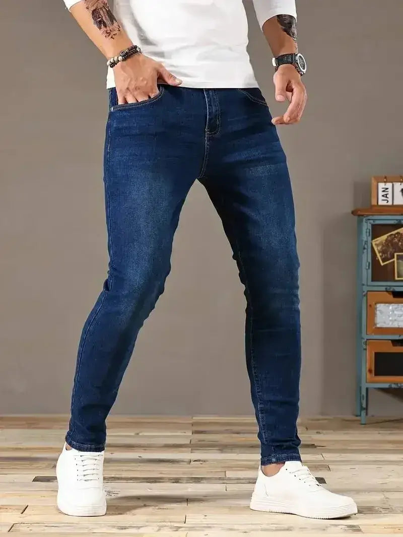 Jeans en denim bleu foncé coupe slim pour homme présentant un design classique à cinq poches et une atténuation subtile pour un aspect porté.