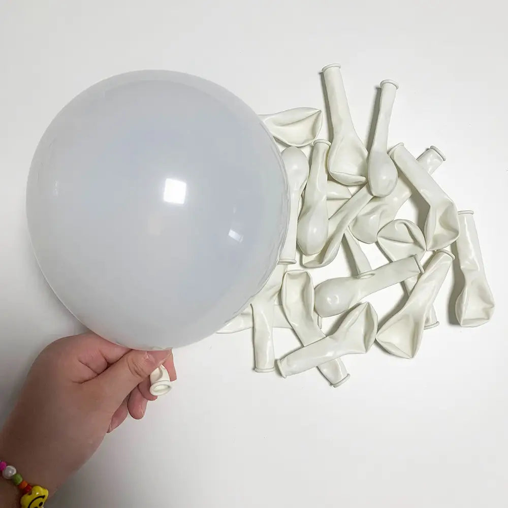 Eine Hand hält einen großen, transparenten weißen Ballon aus einer Partydekoration „Rot Schwarz Weiß Ballon-Set“, mit mehreren entleerten Ballons im Hintergrund.