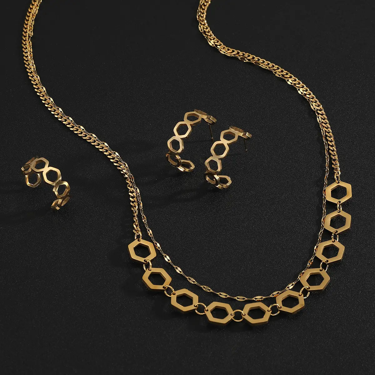 Juego de joyería de acero inoxidable color dorado para mujeres, con un collar de tono dorado con eslabones hexagonales alternados y conectores ovalados más pequeños, acompañado de aretes tipo aro a juego.