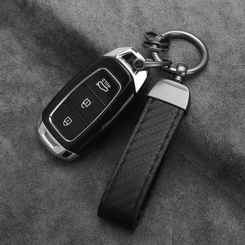 Black carbon fiber car keychain with silver trim and matching leather strap featuring red stitching.