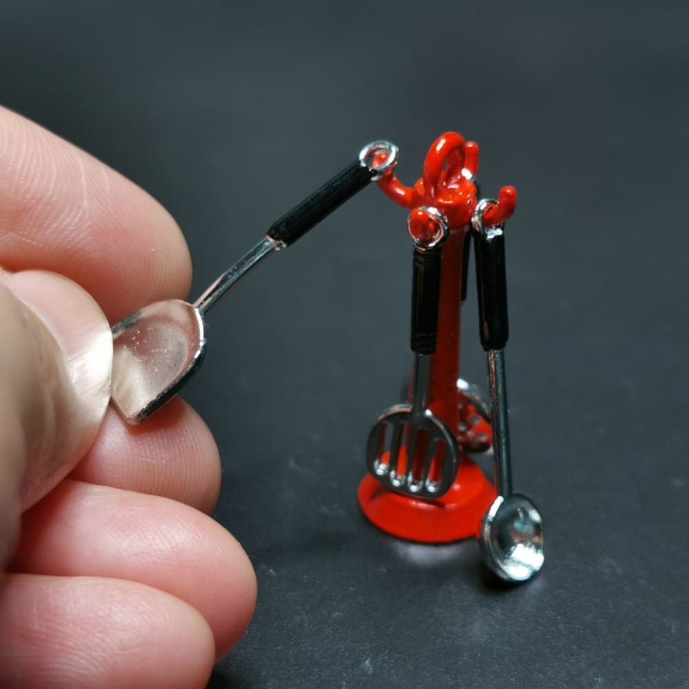 Support en plastique rouge tenant des mini ustensiles de cuisine en métal argenté avec des poignées noires, provenant d’un ensemble d’ustensiles de cuisine miniature pour maison de poupée.