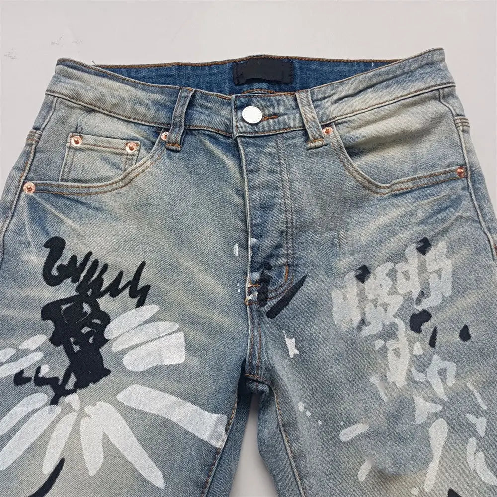 Jeans skinny déchirés pour hommes en denim à lavage clair, avec une œuvre graphique graffiti noire et blanche audacieuse sur les jambes.