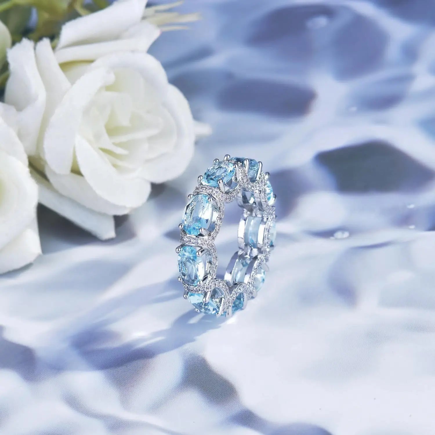 A sparkling silver band ring adorned with oval-cut blue topaz stones and smaller clear accent diamonds from the aquamarine crystal bridal jewelry set.