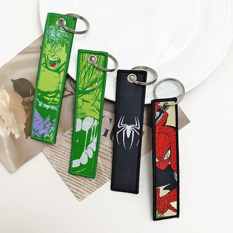 four embroidered superhero keychains featuring green hulk, green and white hulk, black spider-man logo, and red spider-man with metal rings in a superhero embroidered keychain set anime key lanyard