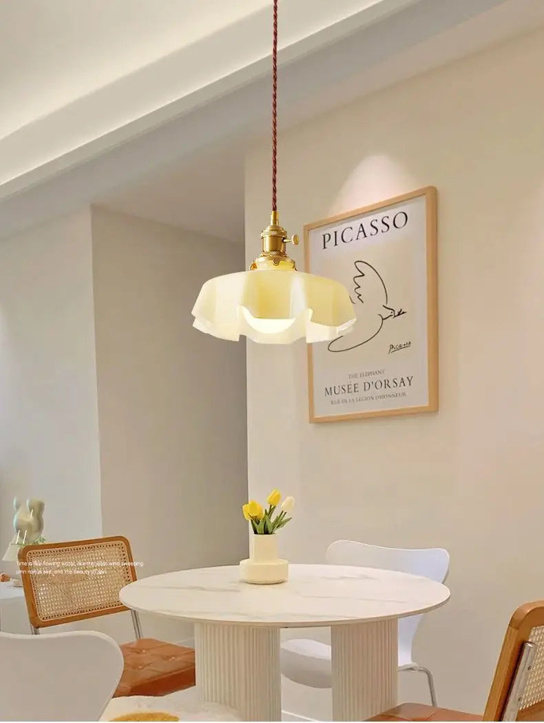 Un luminaire suspendu à jupe florale en verre crème chaud avec une tête de lampe en cuivre et un cordon tressé suspendu au-dessus de la table.