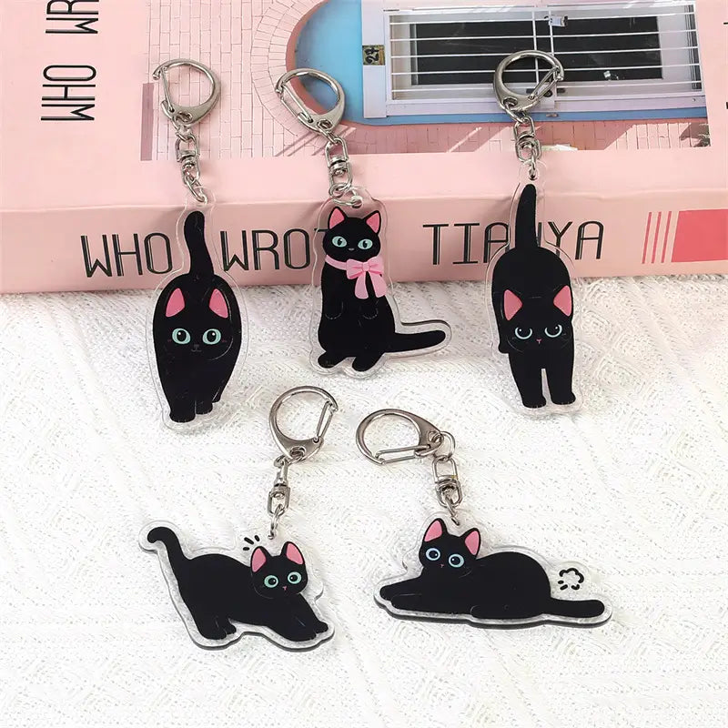 clear acrylic keychains featuring black cats with pink inner ears and blue eyes in various poses designed as cartoon animal bag charms.