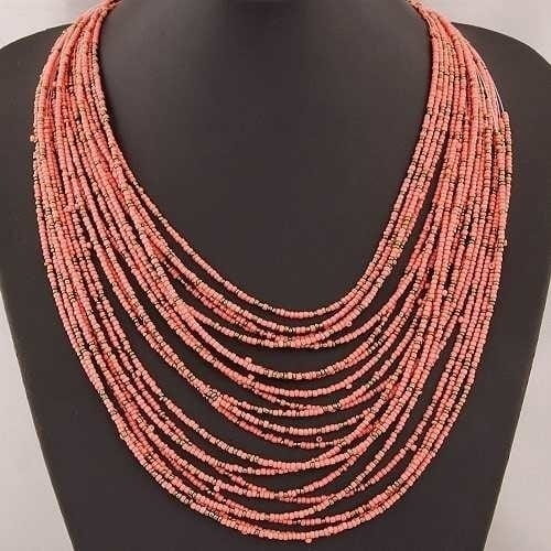 A boho multi-layer bead statement necklace featuring a cascading design of multi-strand coral-colored beads.