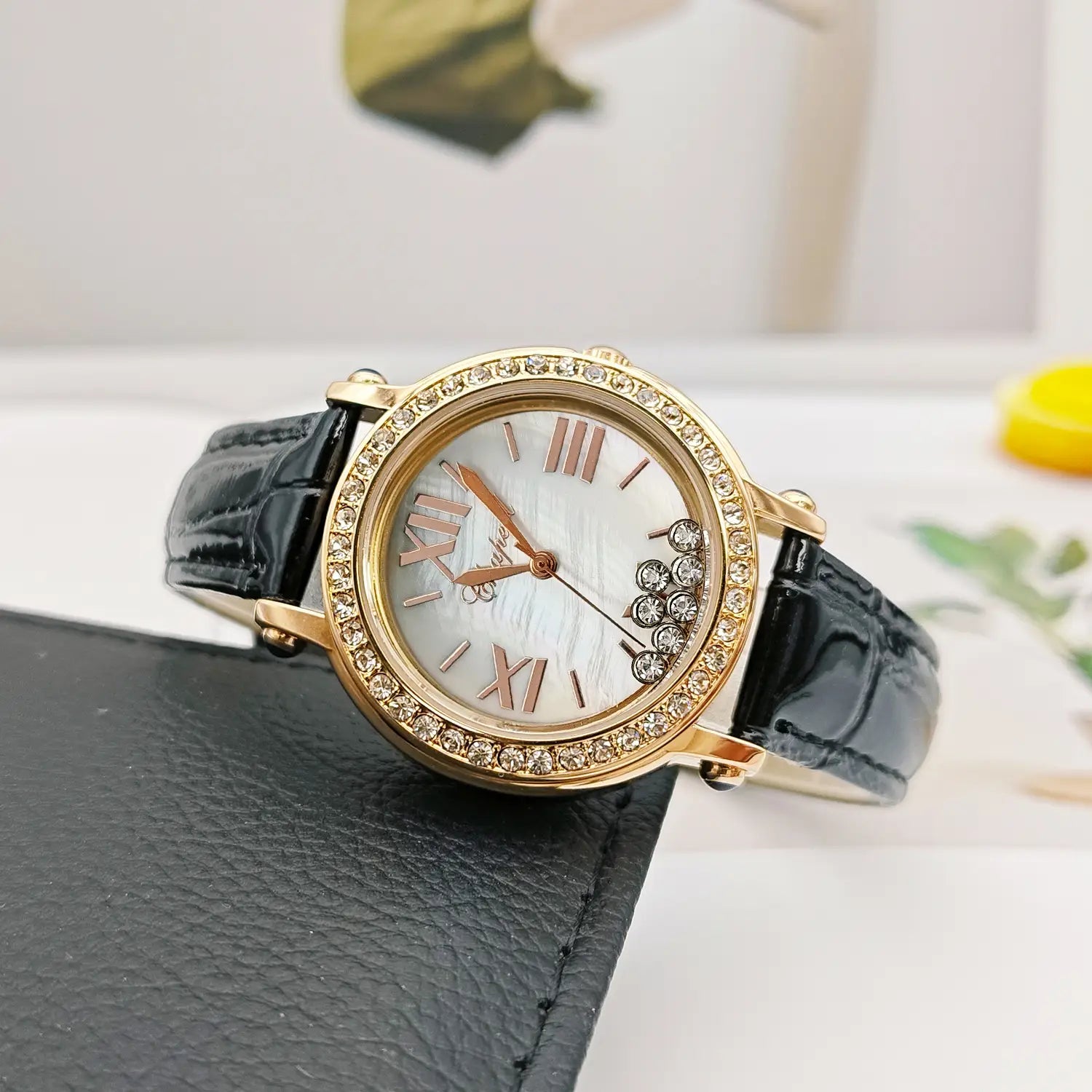 A gold-toned green leather crystal women watch featuring a mother-of-pearl dial with roman numeral hour markers, a clear crystal-encrusted bezel, and a black crocodile-textured leather strap.