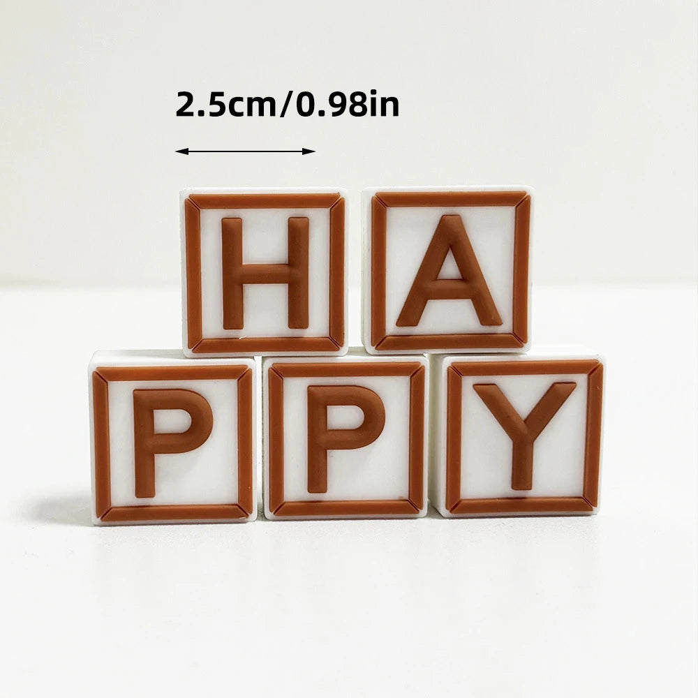 ミニベア ケーキトッパーセットに含まれる、幅2.5cmの白と茶色のプラスチック製レターブロックで「happy」と綴り、2列に配置されています。