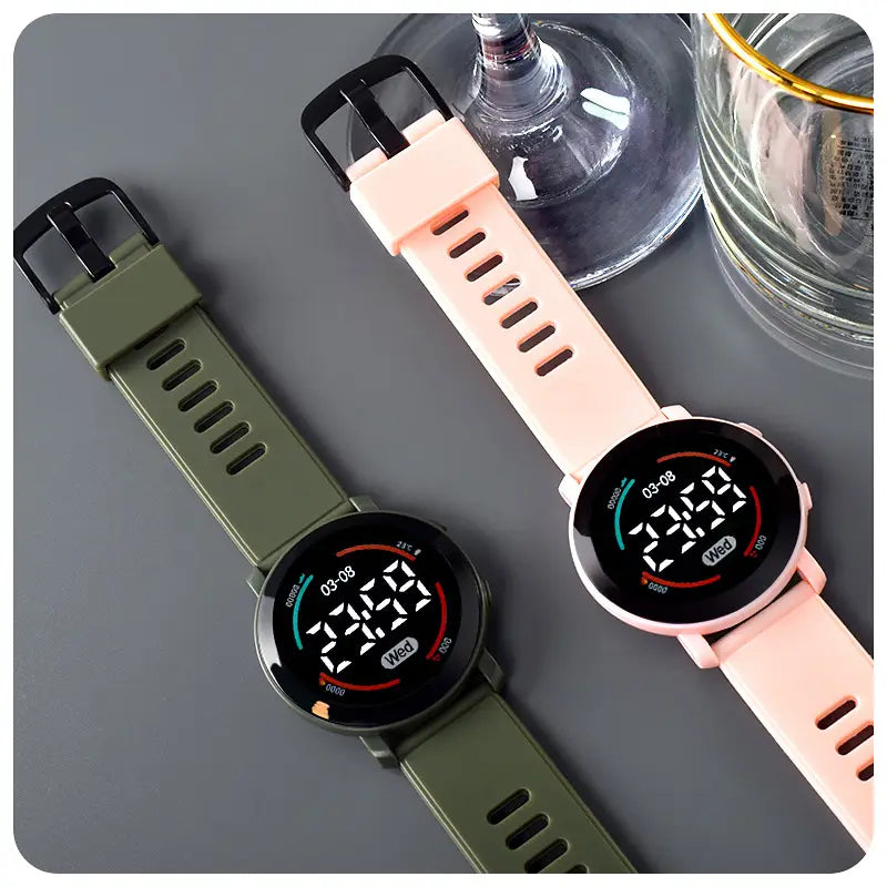 Two girls digital sports watches waterproof led wristwatches with circular faces and sleek black bezels, featuring olive green and soft pink sporty silicone straps displaying time date and temperature.
