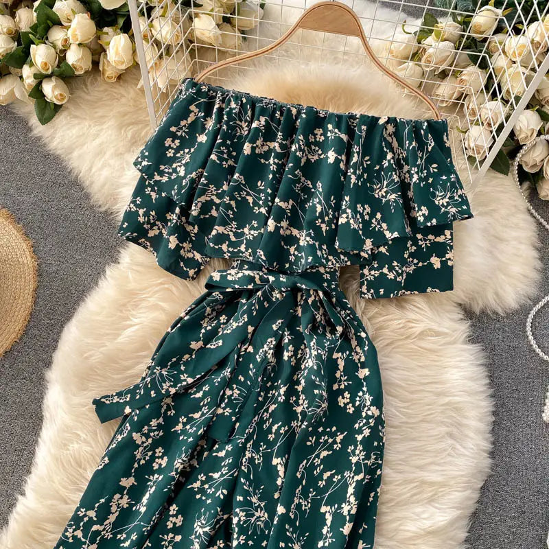 Enterizo de pierna ancha verde esmeralda con escote tipo bardot, con delicado estampado floral blanco y mangas con volante, exhibido en una percha de madera.