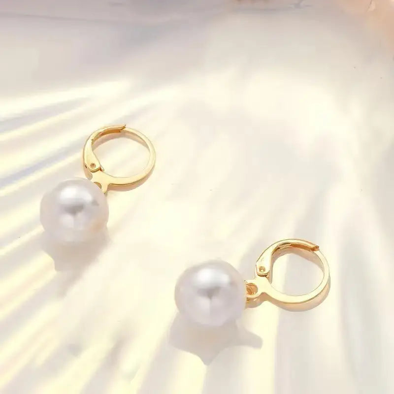 Des boucles d’oreilles créoles dorées avec des perles blanches rondes suspendues à chacune, dans un ensemble de bijoux à collier à pendentif et boucles d’oreilles.