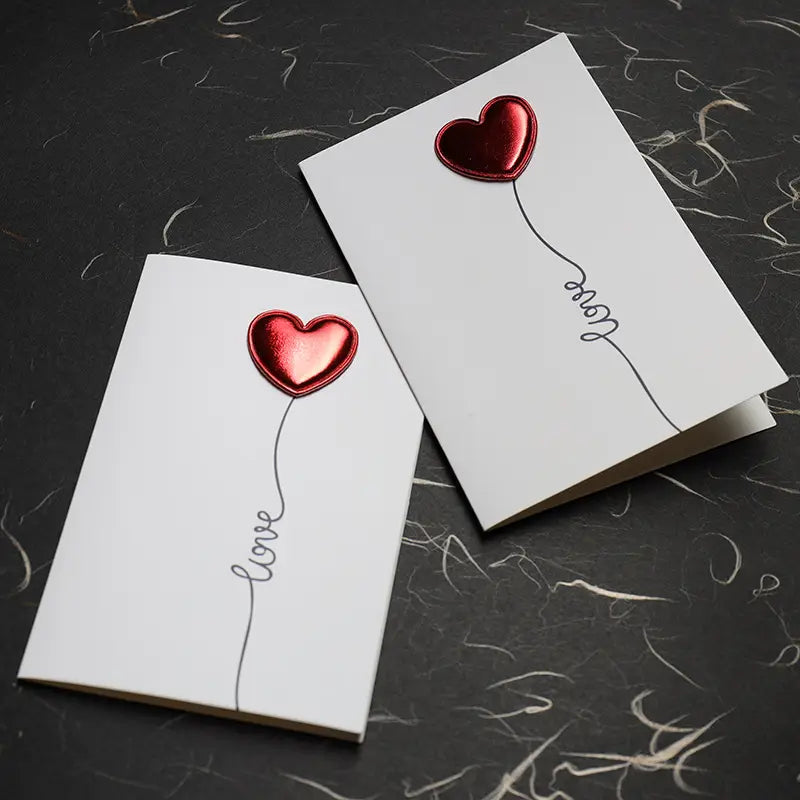 White red heart valentine greeting cards featuring shiny red heart-shaped balloons with the word love written in cursive script along their strings suitable for wedding invitations.