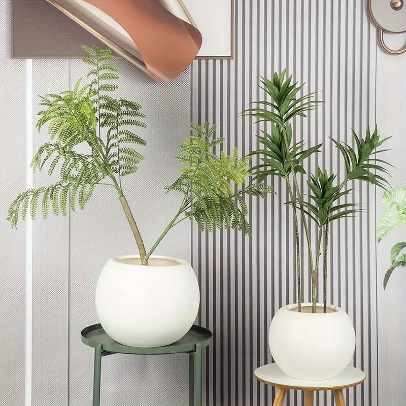 Des pots à fleurs sphériques en plastique léger, de couleur blanche, avec un aspect pierre mate, contenant des fougères vertes artificielles et des plantes à la manière du palmier, pour la plantation de fleurs à domicile ainsi que pour un usage intérieur et extérieur.