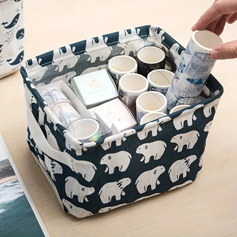 Panier de rangement pliable en tissu bleu marine avec un amusant motif d’ours polaires blancs, rempli de rouleaux de washi tape et de petites boîtes de rangement.