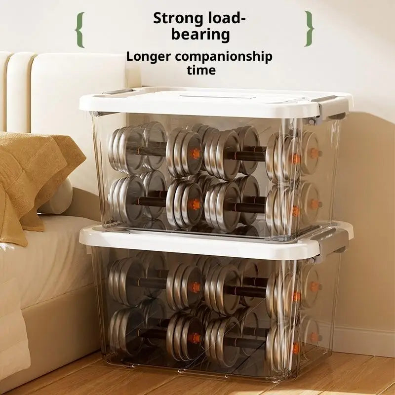 Boîte de rangement en plastique transparent avec couvercle et loquets, en grande taille environ, contenant plusieurs haltères en argent avec des repères de poids orange.