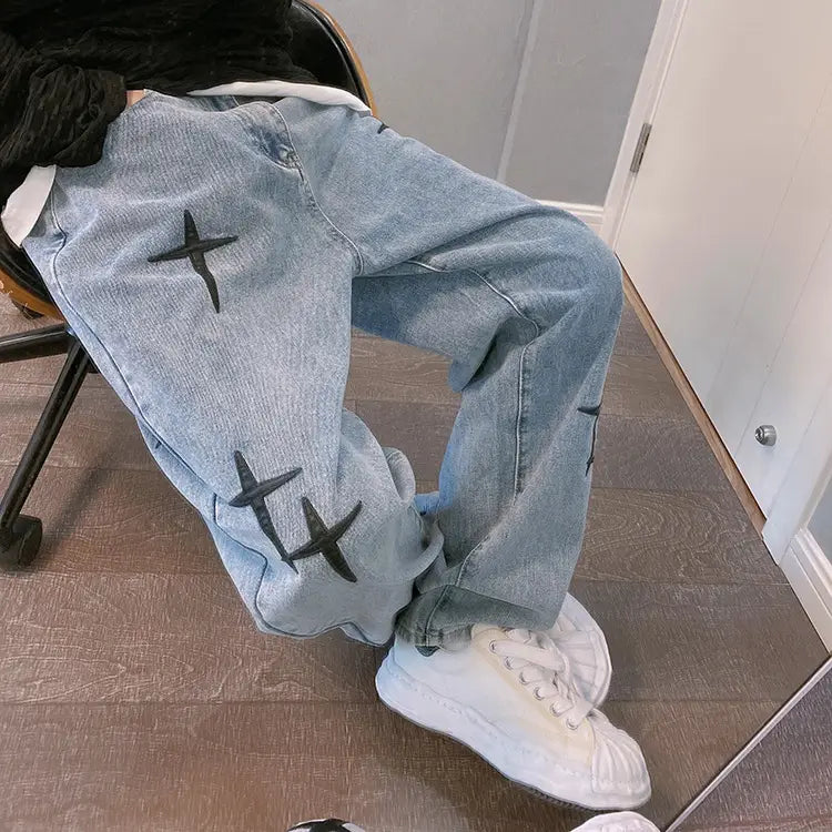 Pantalon cargo en jean à jambes larges à effet délavé clair, avec broderie croisée noire sur les cuisses.