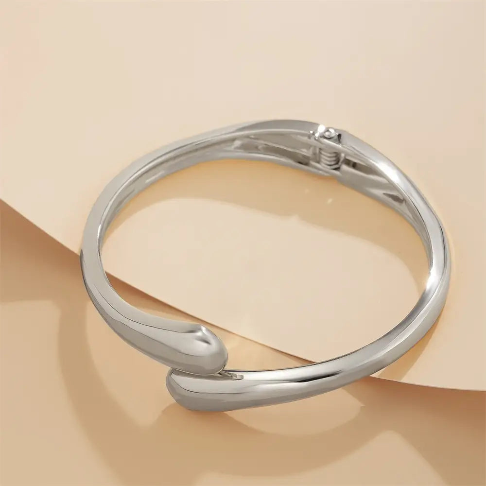 Silver color chunky wide metal bangle with a sleekly curved minimalist design and spring clasp in metal material.