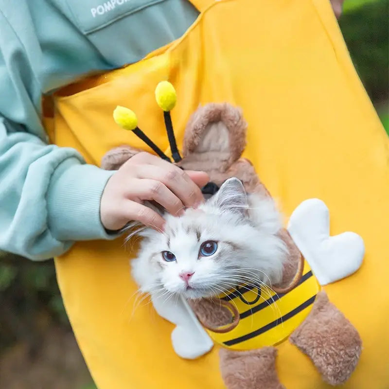 fluffy white cat wearing a plush bee costume with yellow and black stripes and brown wings sitting next to a canvas pet carrier bag with cartoon animal print designed for small dogs and cats including mouth length dimension for comfortable use