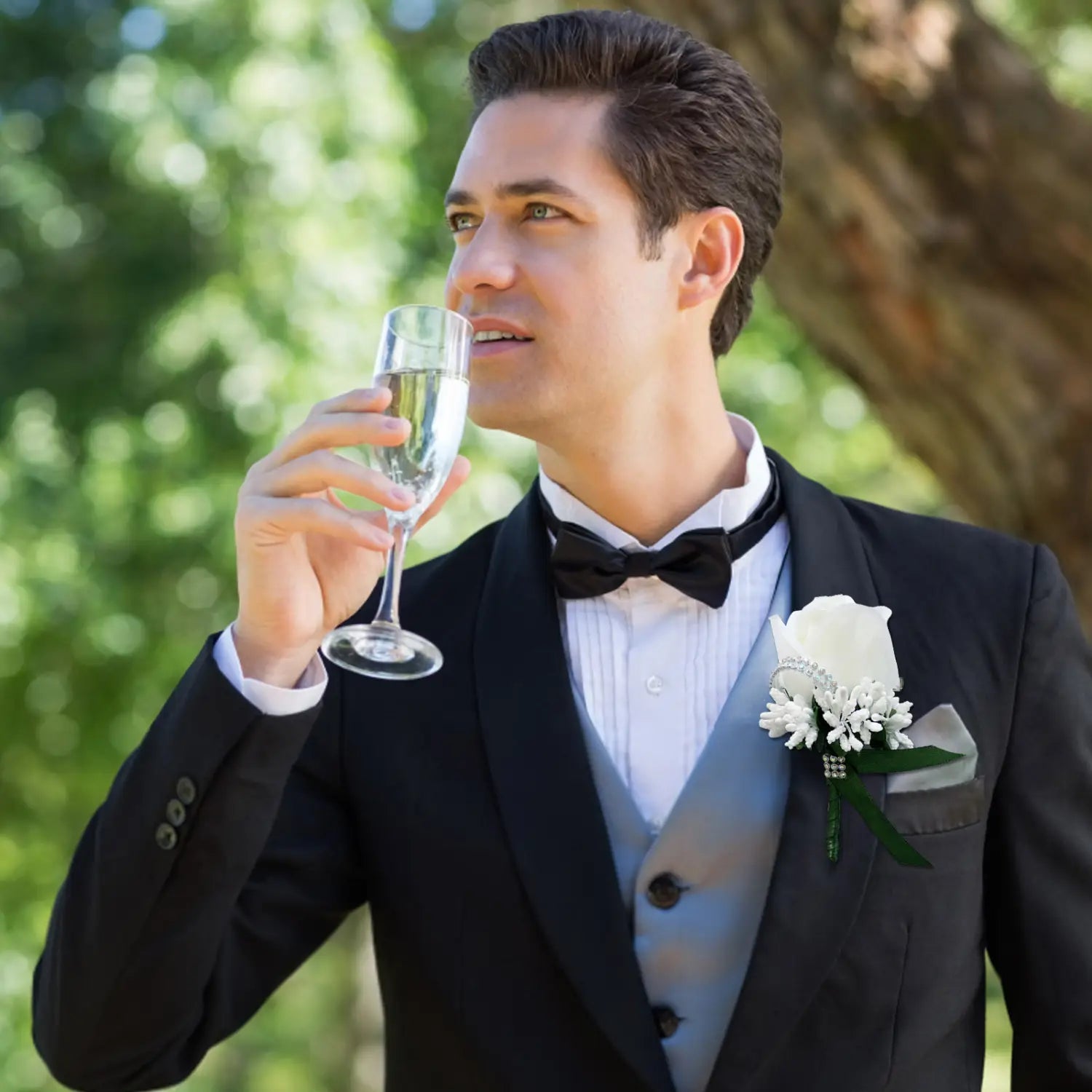 A clear elegant champagne flute held delicately in a mans hand alongside a blue wedding boutonniere artificial silk rose corsage.