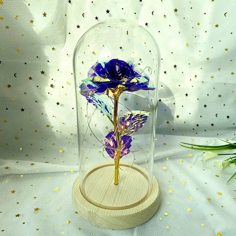 Eine schimmernde blaue und goldene metallische Rose, umschlossen in einer klaren Glaskuppel, mit LED-Licht auf einem hellen Holzsockel, für ein „Eternal Gold Rose Glass Dome LED Light Gift“.