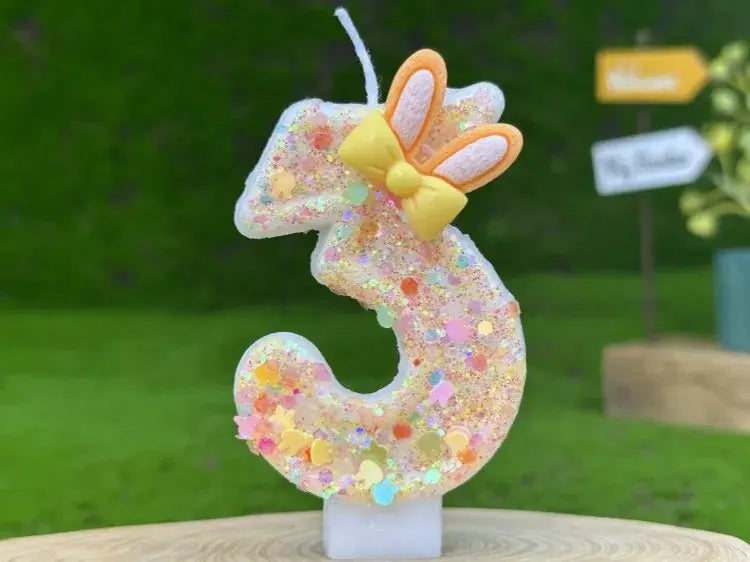 a glitter bunny ear number birthday candle featuring a glittery translucent number three adorned with a yellow bow and orange bunny ears.