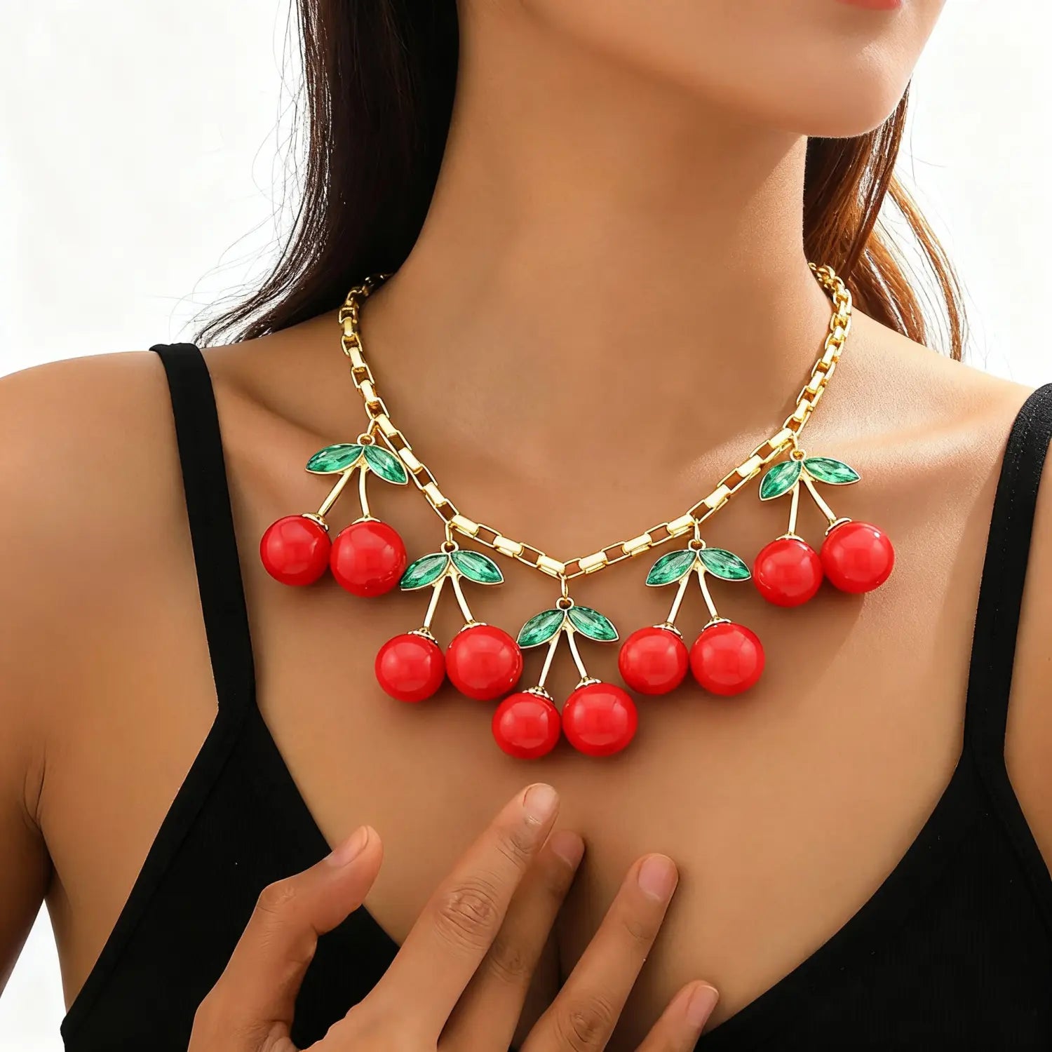 Un collier ras du cou composé d’une chaîne dorée audacieuse, doté de pendants cerises rouges éclatants et de feuilles vertes lustrées, mettant en valeur un design de collier ras du cou en cristal.