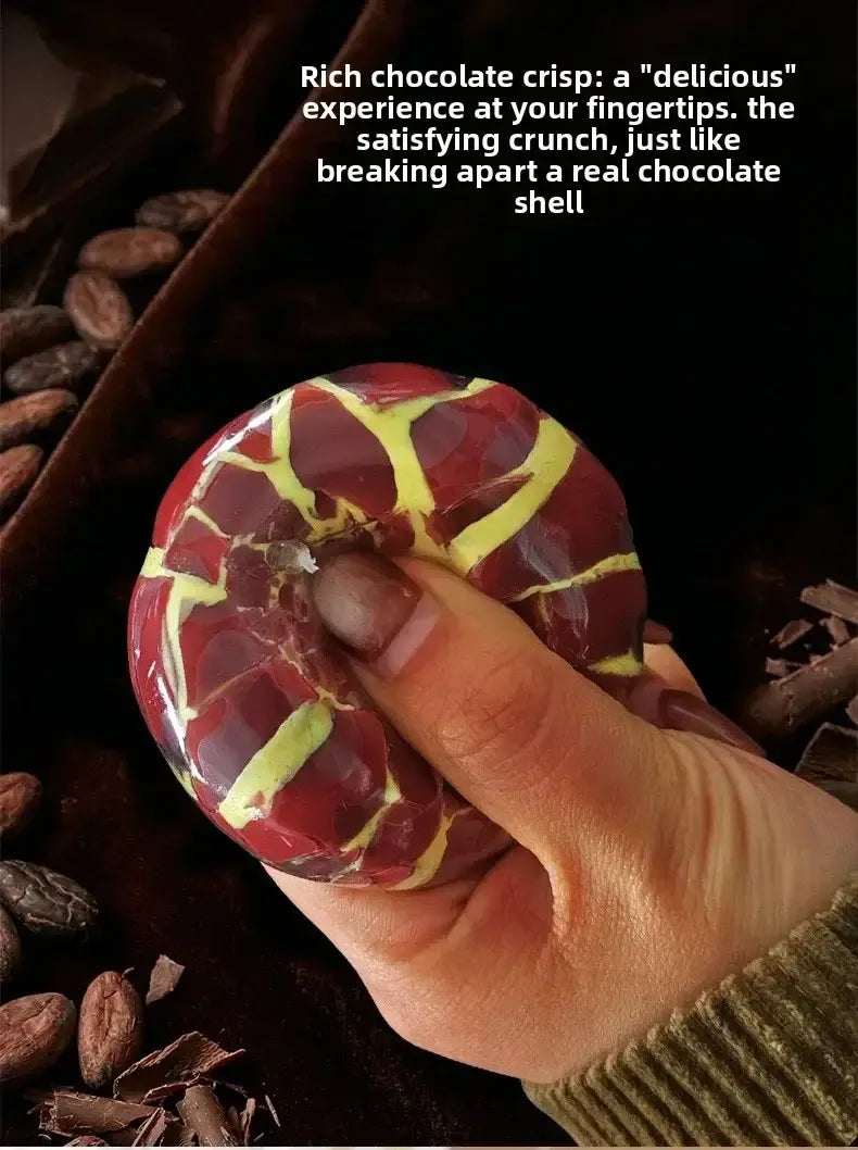 Una esfera antiestrés con piel de cera esponjosa y crujiente, con una cáscara brillante de color chocolate granate y amarillo, deshecha en partes mediante un dedo.
