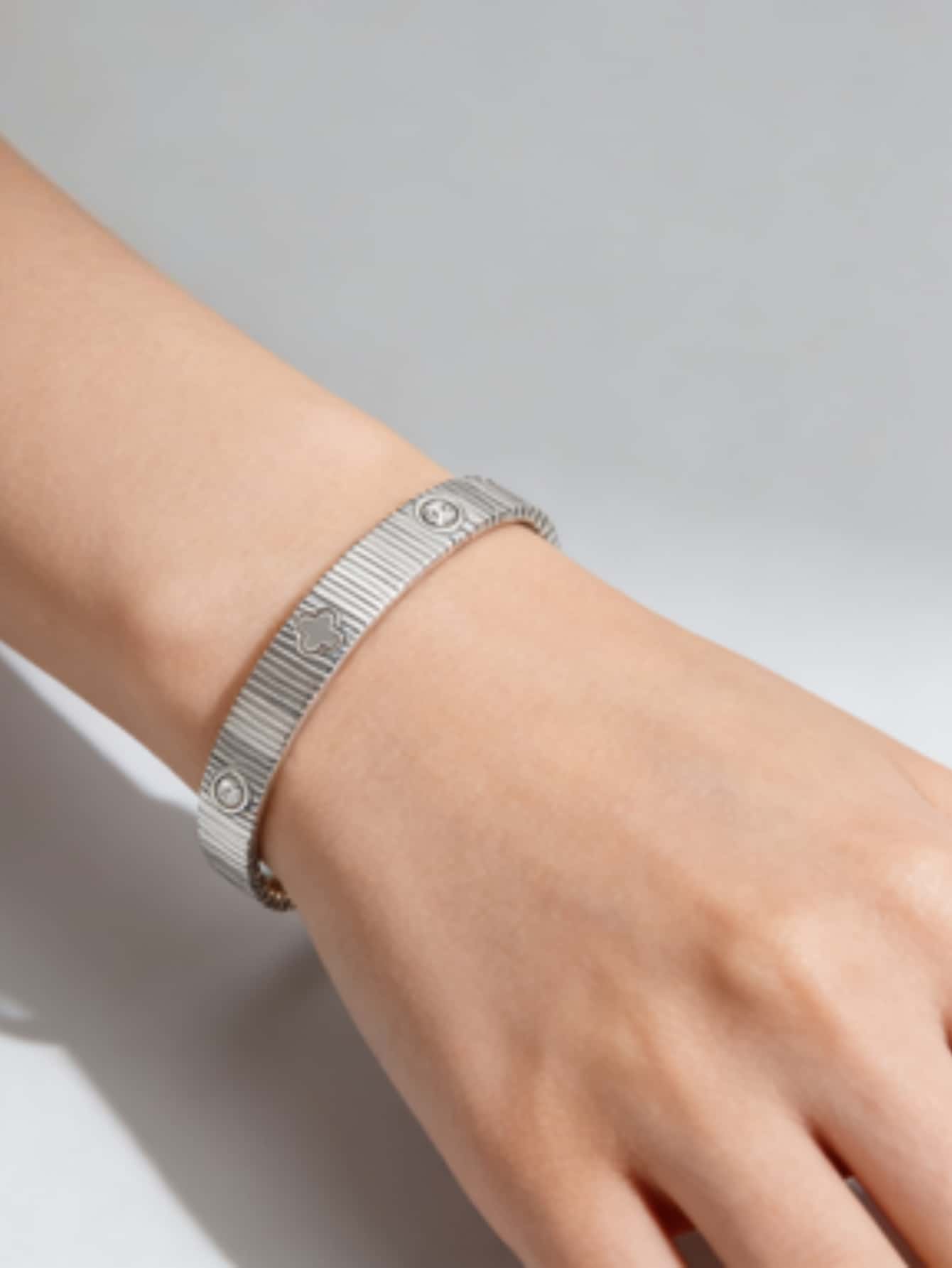 Pulsera tipo brazalete con cruz de metal con acabado plateado, diseño acanalado con textura y pequeños motivos de corazón grabados.