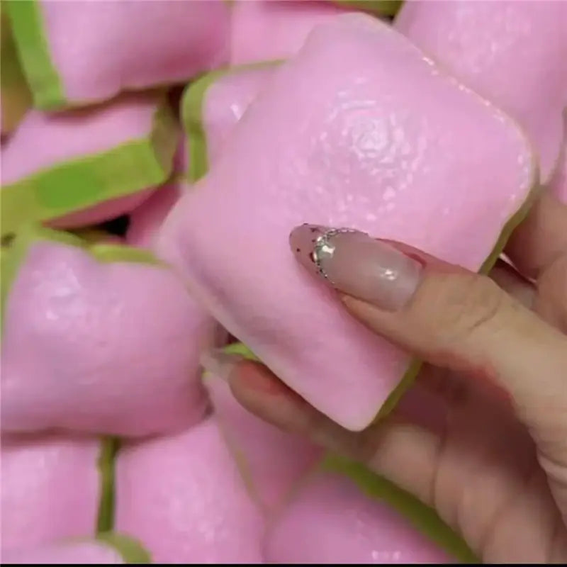 Butterstick als ASMR-Sensory-Squishy-Spielzeug in Form eines pinkfarbenen quadratischen Marshmallows mit glatter Oberfläche und grün wirkenden, blattartigen Rändern; entworfen für taktiles Spiel und Stresslinderung.