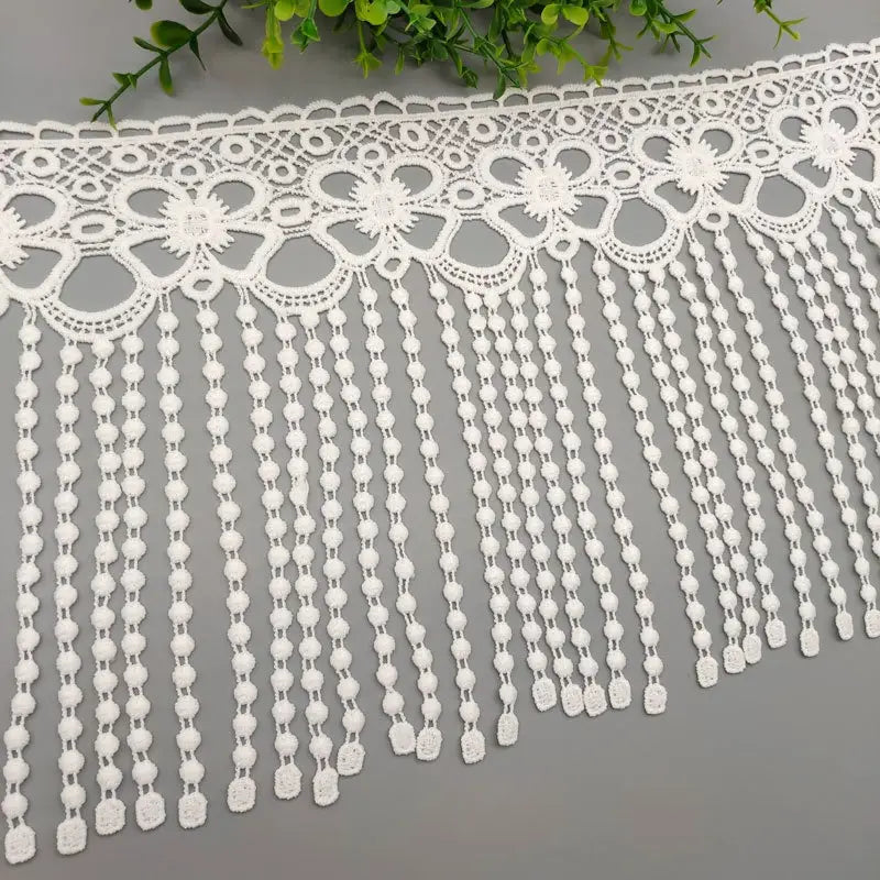 Tissu à bordure de dentelle à perles blanches, présentant des motifs de dentelle florale blanche avec un détail de frange de perles.