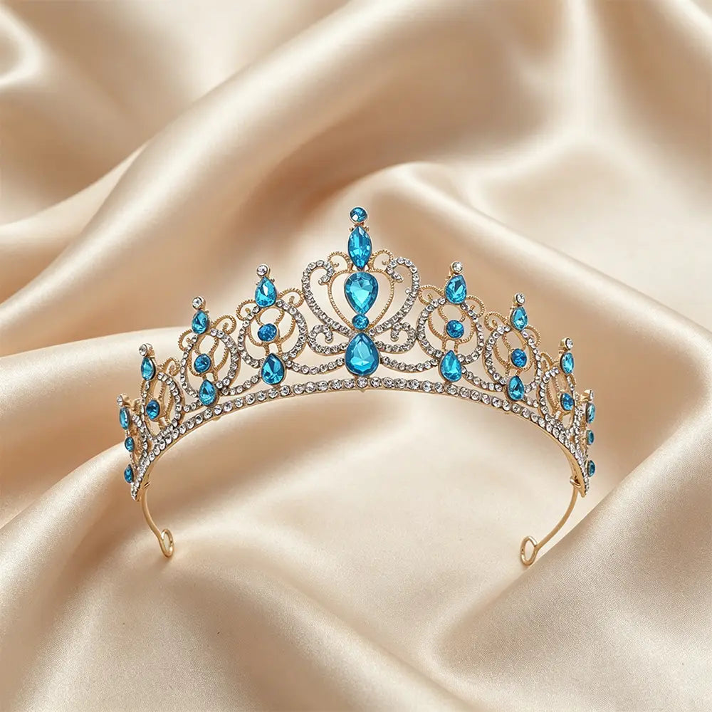 Une délicate couronne de diadème baroque en strass doré, ornée de cristaux en forme de goutte bleus étincelants et de plus petits strass transparents, disposés sur un fond de satin doux, destinée à un usage d’accessoire de coiffure de mariée.