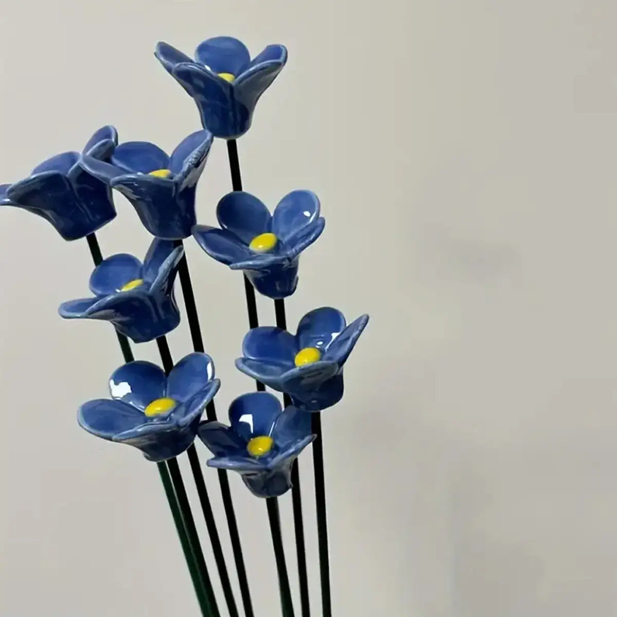 Artificial flowers blue ceramic forget me nots with yellow centers on black stems ideal for decorating vases.