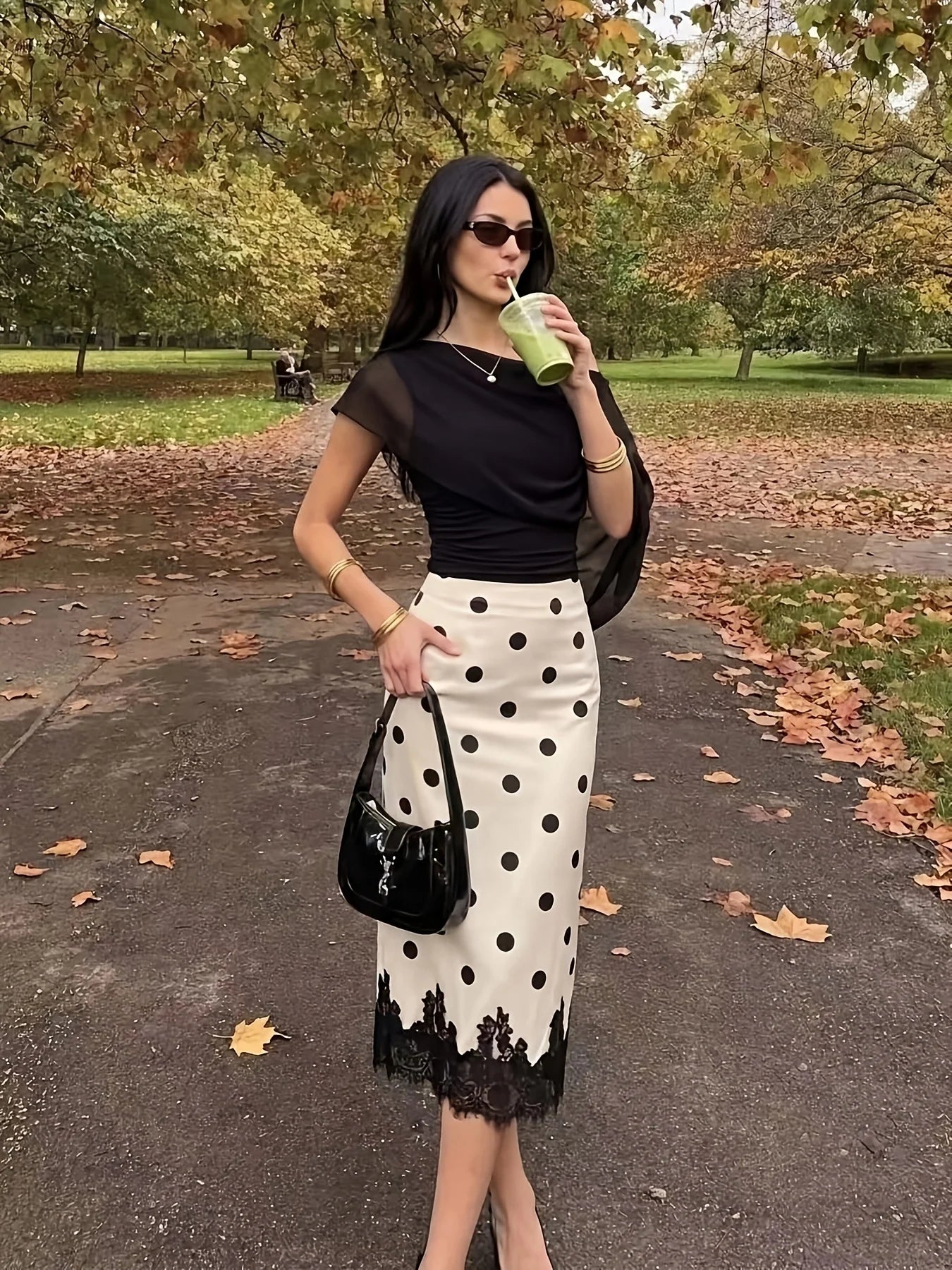Bolso de mano YSL de cuero charol negro con acabado brillante, presentado junto con una falda midi de encaje con lunares.