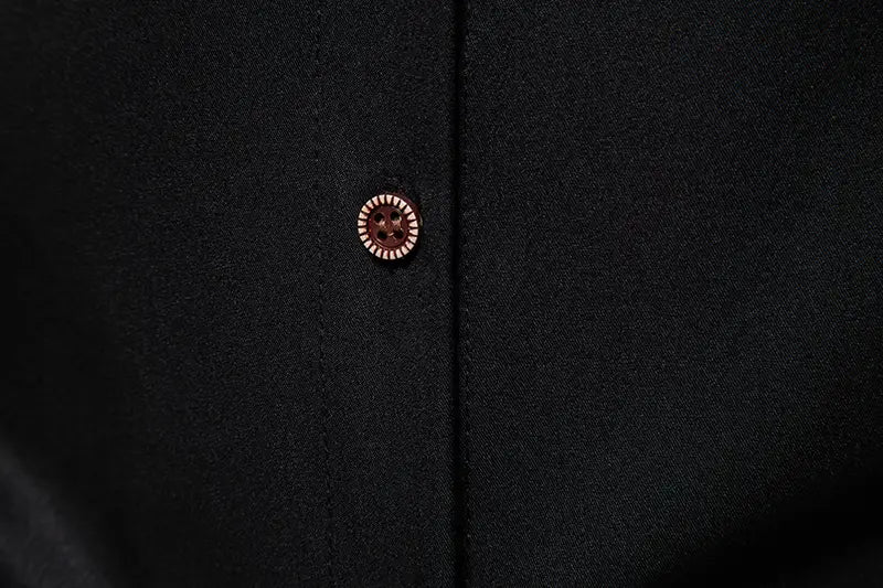 A round rose-gold button with a textured ridged edge and dark center on a men asymmetrical slant collar long sleeve casual shirt against black fabric.