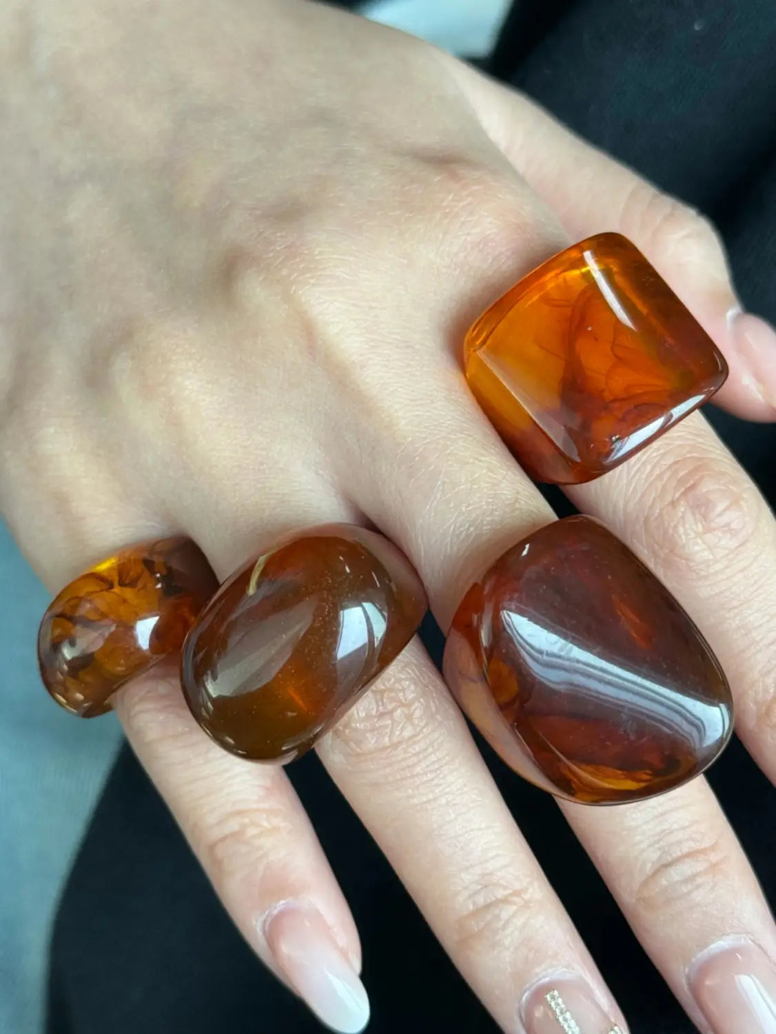 a set of three amber-colored chunky resin cocktail rings with polished smooth rounded edges and natural marbled patterns