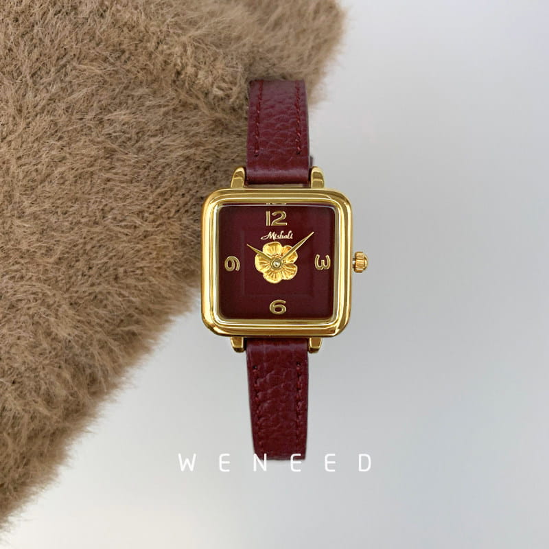 A square women quartz watch with a burgundy leather strap and gold-tone case featuring a floral design at the center of its face.