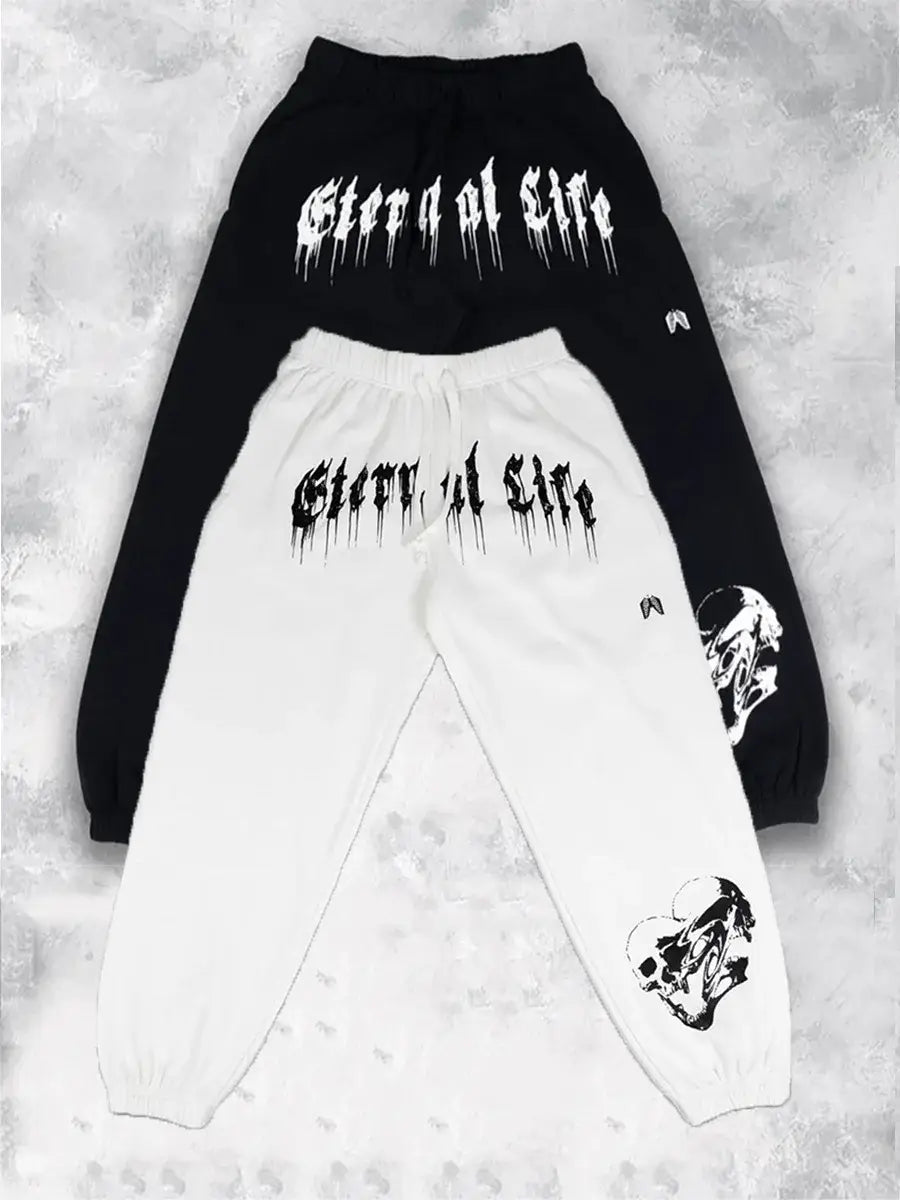 Pantalons d’entraînement graphiques pour hommes, sweatpants noirs et blancs, avec la mention « sleep at the » dans une police gothique qui s’écoule, sur l’avant, et des graphismes de crânes sur chaque jambe.