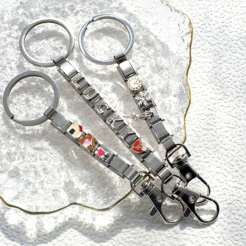 Tres llaveros con dije de eslabones italianos con acabado plateado presentan eslabones metálicos entrelazados con dijes esmaltados de colores, y uno con una carátula de reloj en miniatura para uso personalizado en bricolaje.