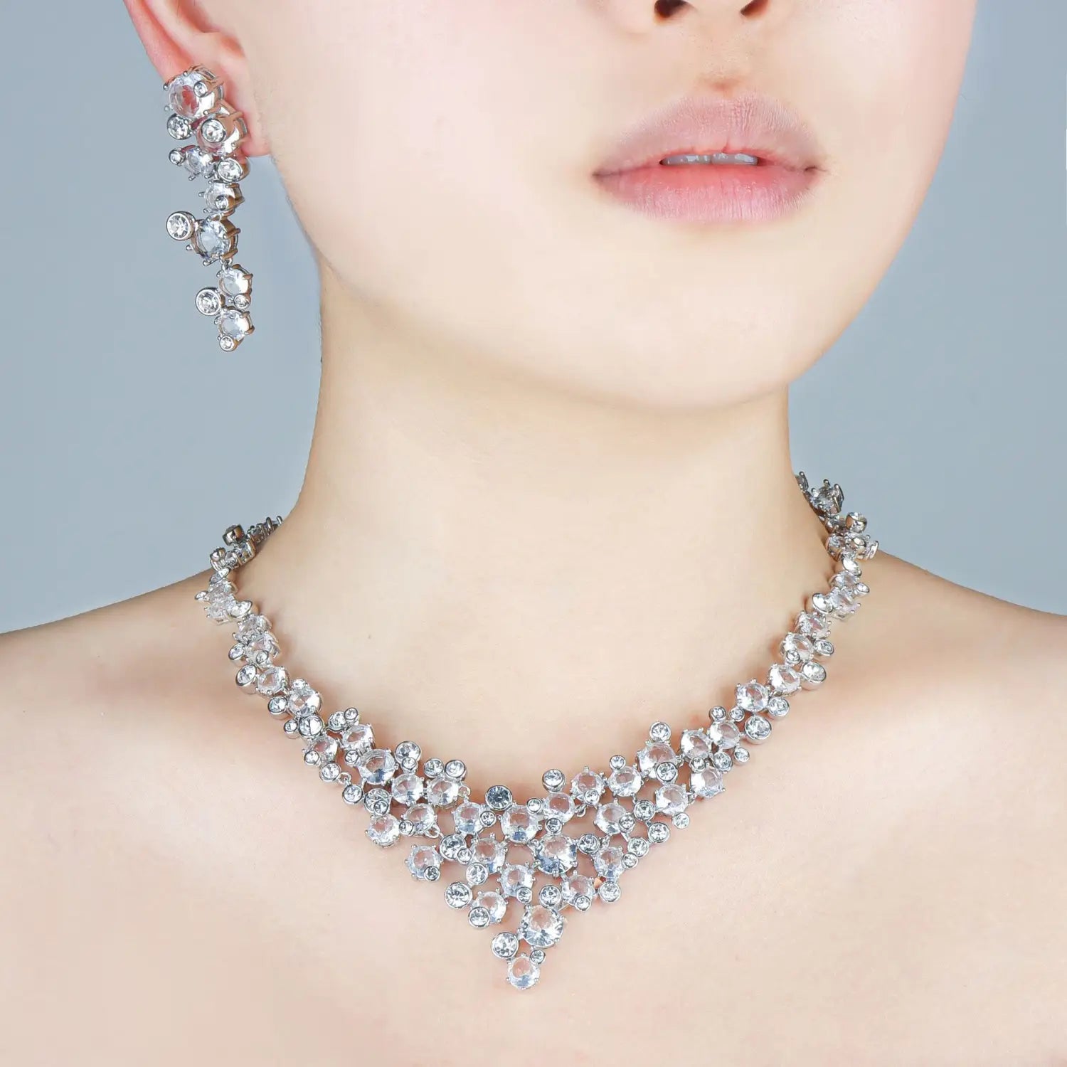 Un collier ras du cou en argent éclatant, en forme de gouttière, orné de cristaux transparents en cascade et de travail métallique délicat, issu de l’ensemble de bijoux de mariage en cristal, collier en argent et boucles d’oreilles.