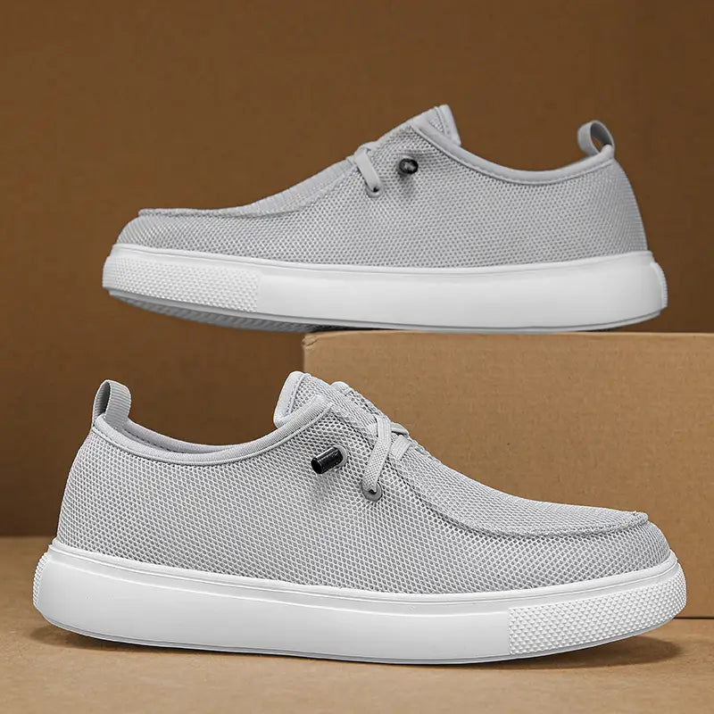 Chaussures de type mocassins décontractées pour hommes en gris clair, avec une tige en maille respirante, des semelles en caoutchouc blanc et des œillets noirs.