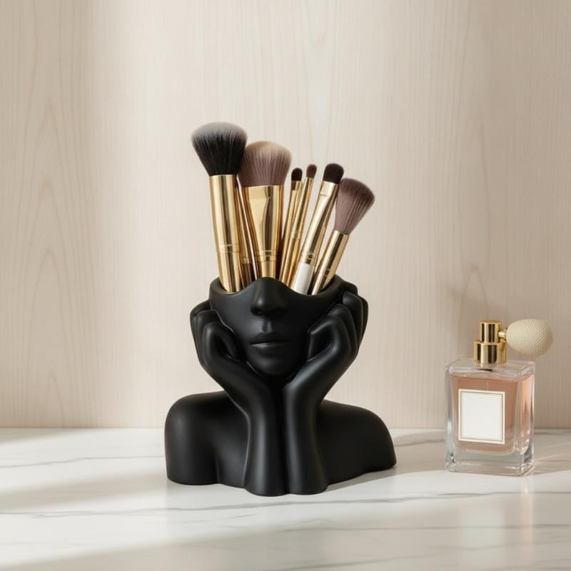 Black sculpted ceramic abstract face makeup brush holder with hands framing the cheeks holding multiple brushes with gold ferrules and soft bristles.