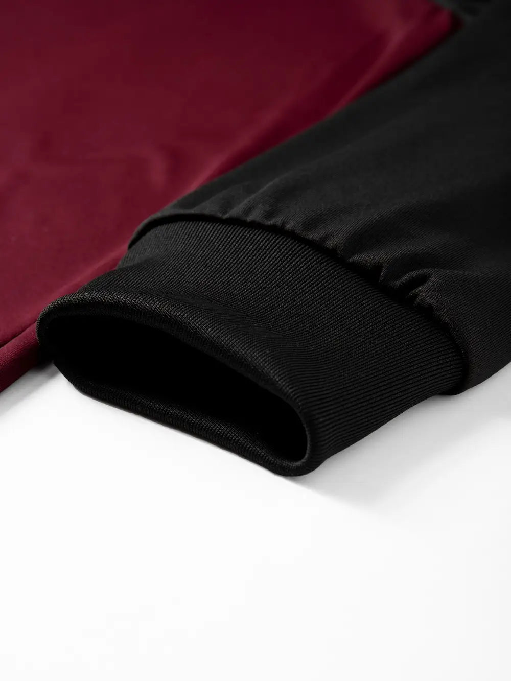 Das Ärmelbündchen eines Herren-Raglanshirts mit langem Ärmel, aus geripptem Strickmaterial, mit bordeauxroten und schwarzen kontrastierenden Farbpaneelen.