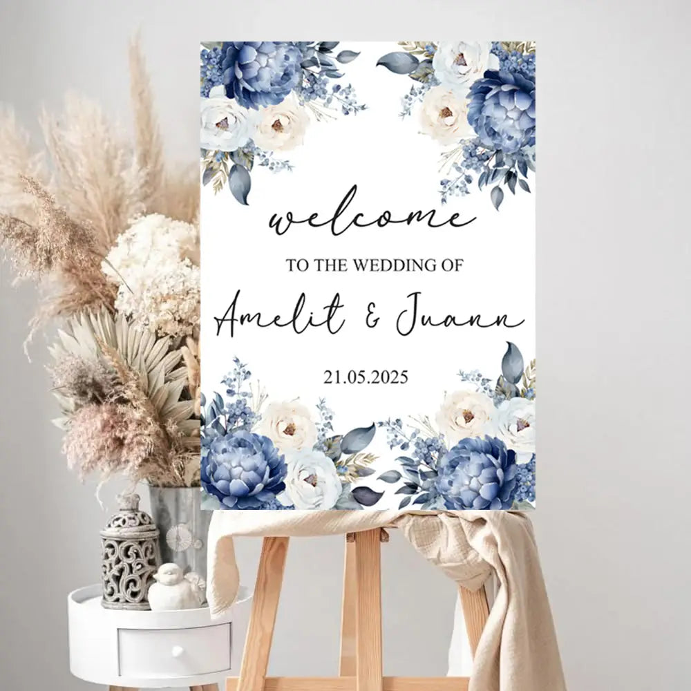 Un panneau d’accueil de mariage sur mesure sur un support rectangulaire en mousse blanche, comprenant un texte personnalisé et encadré par des fleurs style aquarelle bleu et crème dans les coins