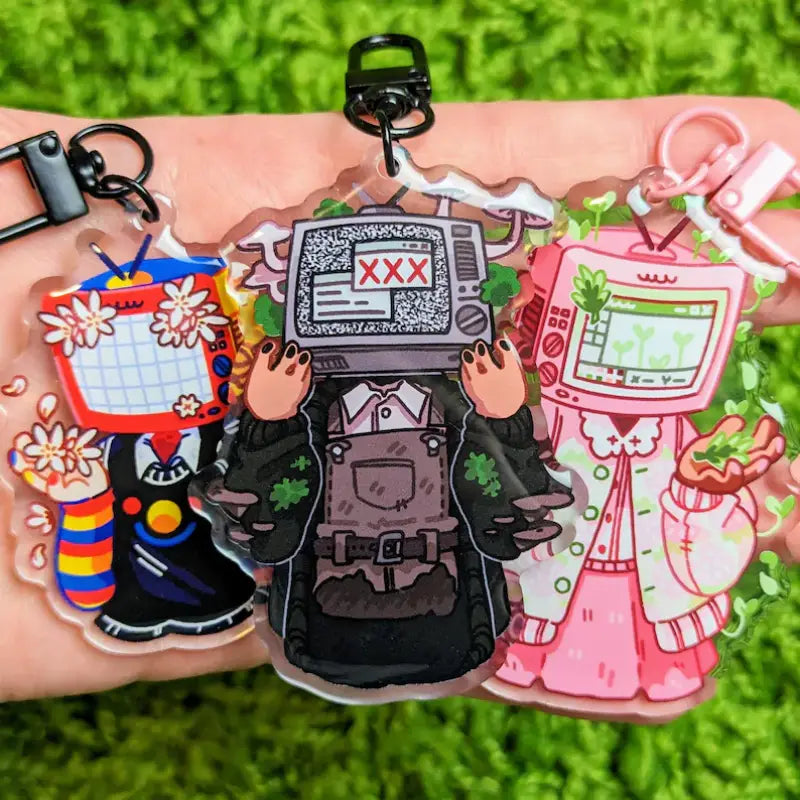 three colorful cartoon-style acrylic tv head anime keychains with retro characters featuring floral and pixelated designs customizable as bag charms