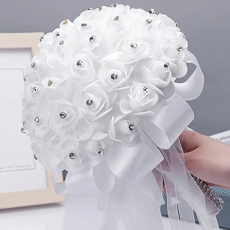 人工の白いバラにきらめくラインストーンをあしらった、装飾的なラインストーンの結婚指輪リングピローのフローラル・ブライダルブーケの土台に、白いサテンリボンをリボン状に結んだ、繊細な一品です。